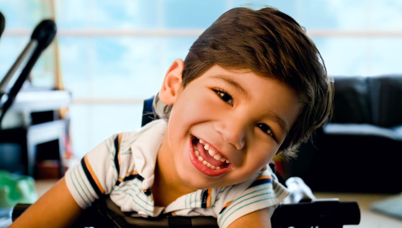 Boy with CP smiles while propped up in a chair