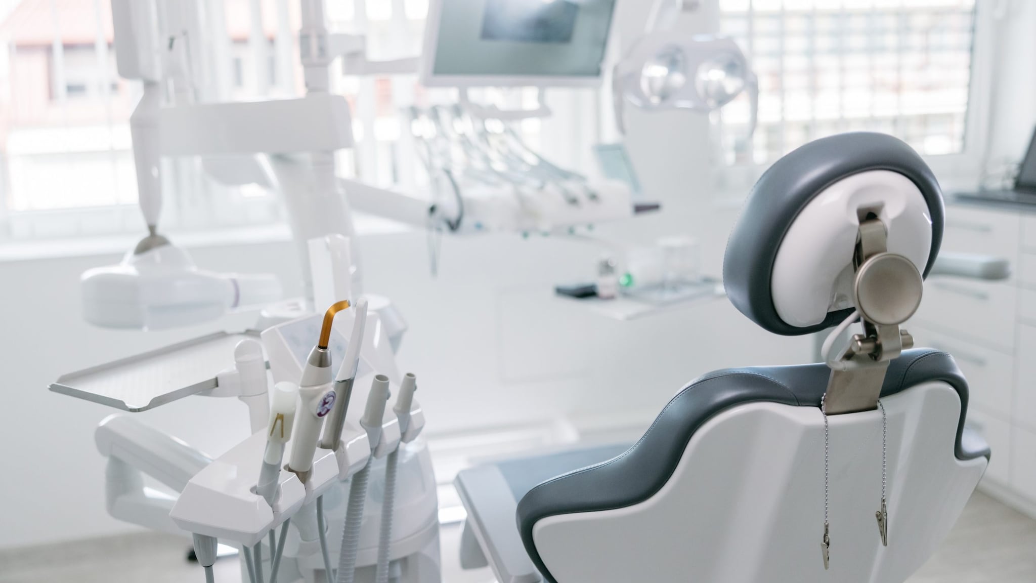 A white room with a blue dental chair and dental handpieces to the left of the chair.