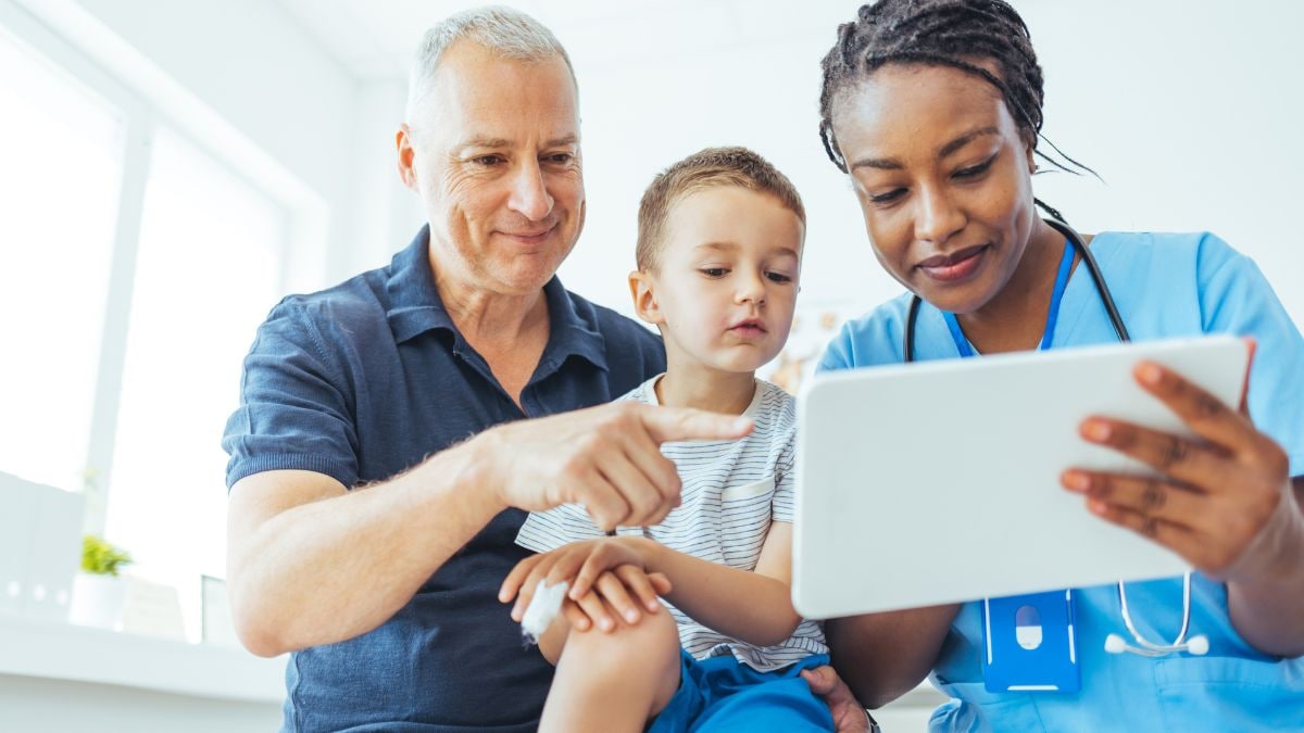 A father and young child talking to a healthcare professional and looking at a tablet screen