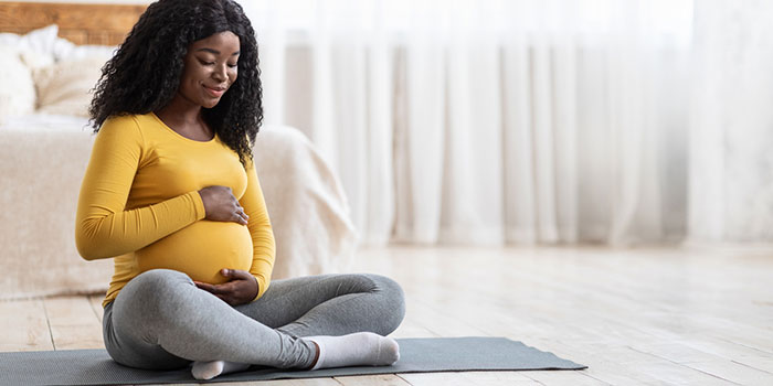 Pregnant woman sitting on yoga mat, holding belly and smiling