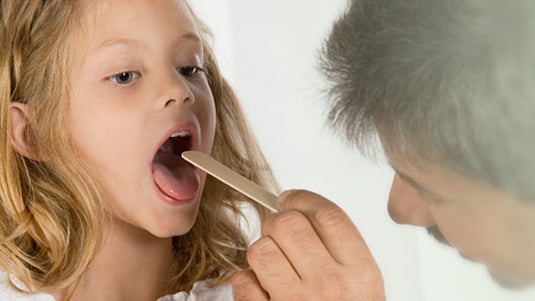 A healthcare provider examining the throat of a young girl.