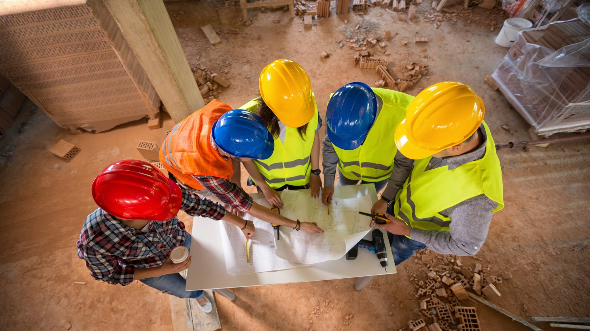 five people in hard hats standing looking at plans together