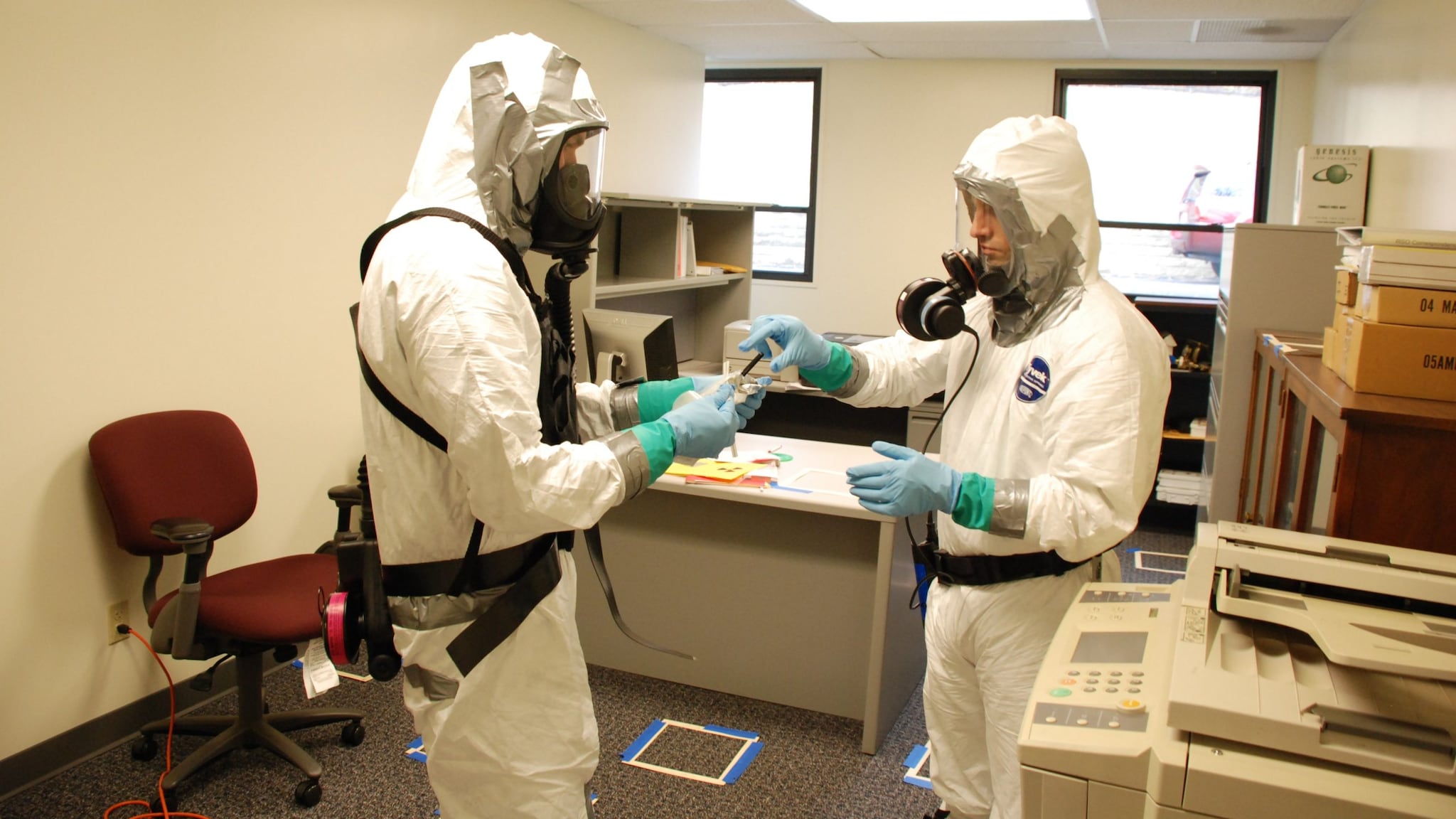 two workers wearing white protective suits and blue gloves