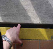 Persona con el dedo apuntando hacia abajo a una separaci%26oacute;n grande entre las baldosas de un pasillo exterior