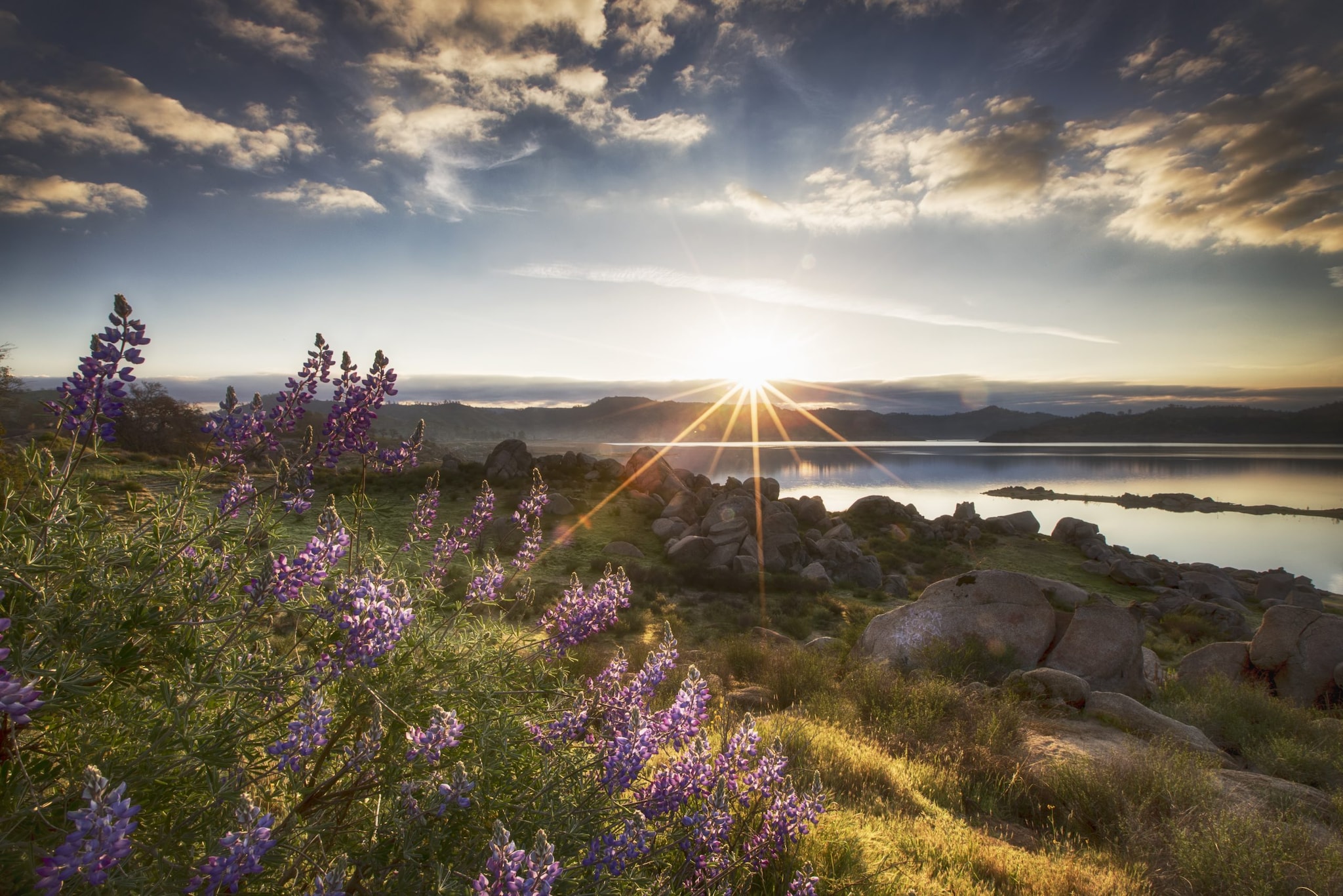 A sunbeam shining over a landscape of mountains, water, rocks, and flowers